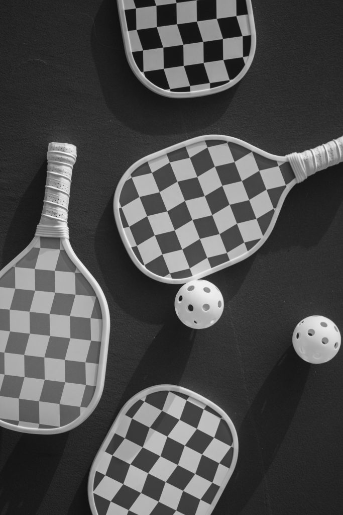 Checkered pickleball paddles and balls on a dark background, viewed from above.