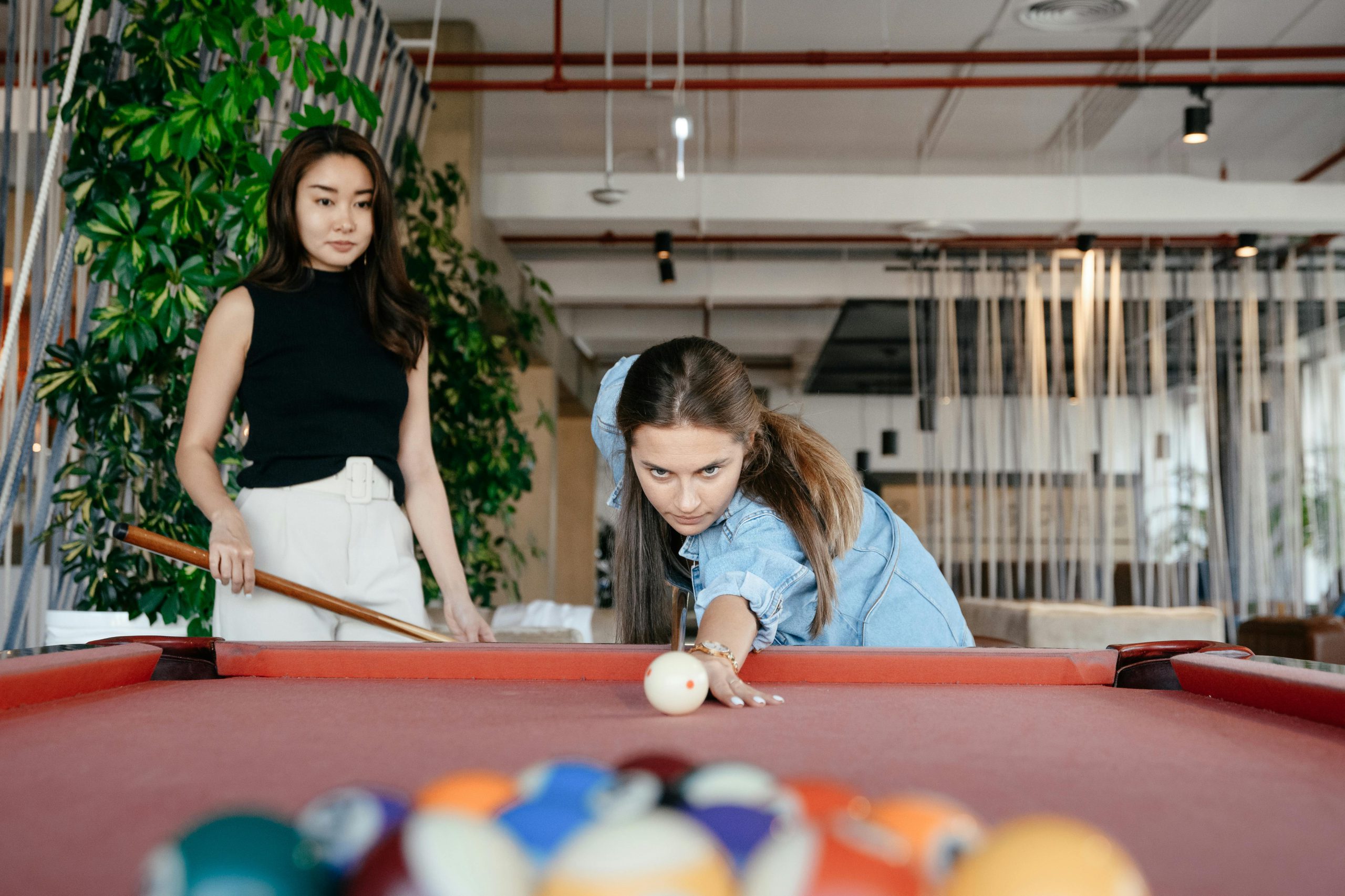 Two women playing billiards in a stylish indoor lounge, focused and enjoying leisure time.